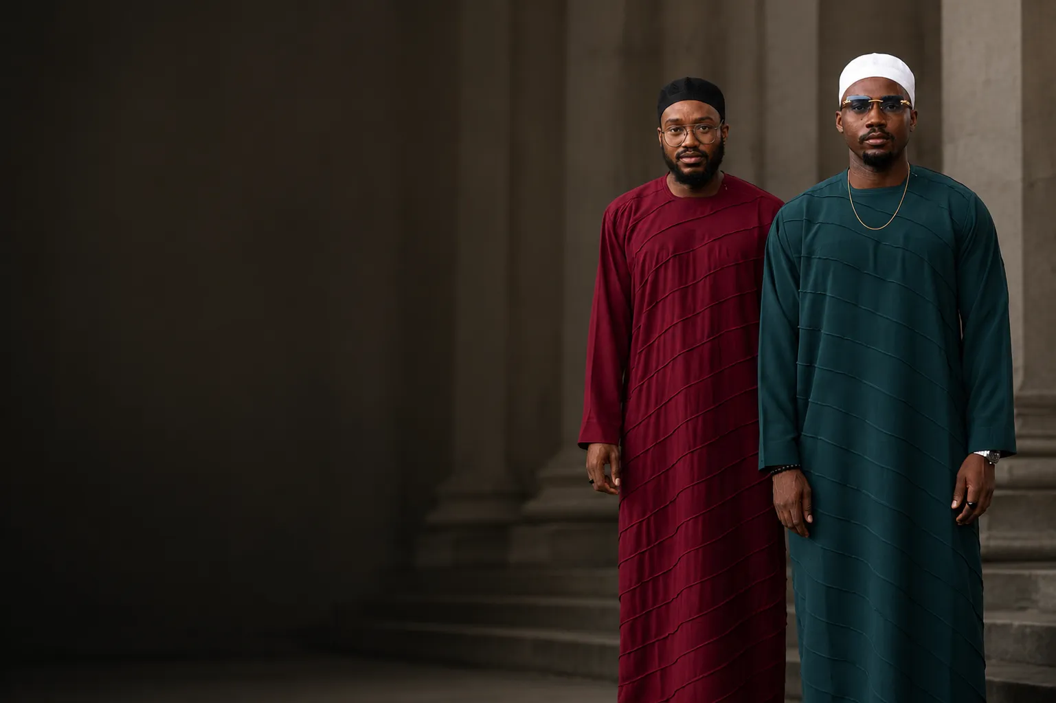 Two men in wine and teal jalabia standing among architectural columns