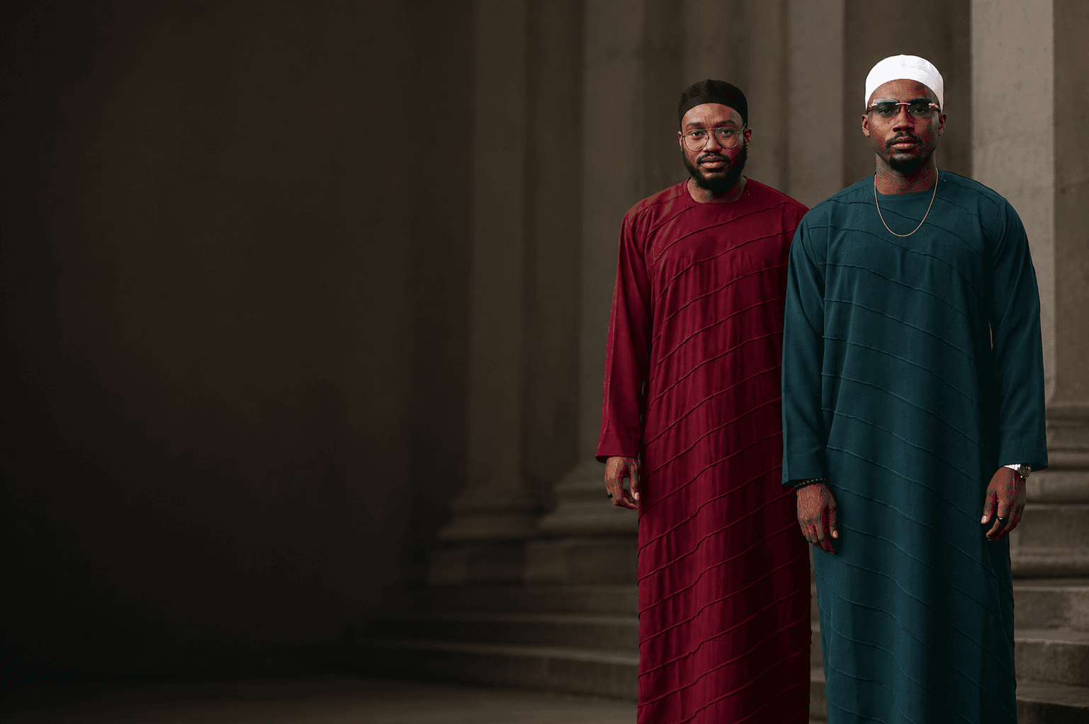 Two men in wine and teal jalabia standing among architectural columns